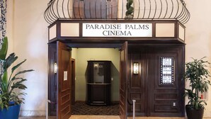 The entrance to Paradise Palms Cinema with a sign above the doors, a ticket booth, and potted plants. - Golden Hours at Paradise Palms (Kissimmee)