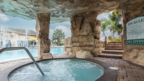 A spa area with a hot tub, a sign listing spa rules, and a pool with a waterfall. - Golden Hours at Paradise Palms (Kissimmee)