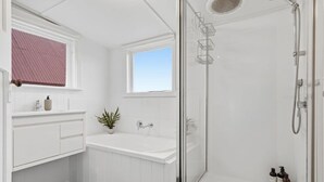 A modern bathroom with a glass-enclosed shower, a white vanity with a sink, and a window providing natural light. - Dellara Cottage Retreat (North Hobart)