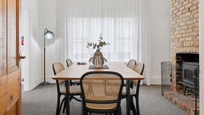 A dining area with a wooden table, six chairs, a vase with flowers, a floor lamp, and a brick wall with a fireplace. - Dellara Cottage Retreat (North Hobart)