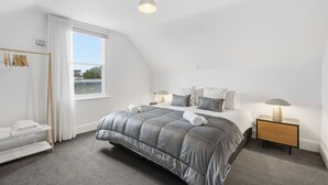 A bedroom with a large bed, bedside lamps, a window, and a radiator. - Dellara Cottage Retreat (North Hobart)