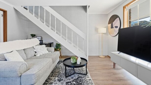 Ett vardagsrum med en trappa, en soffa, ett soffbord, en tv och en golvlampa.