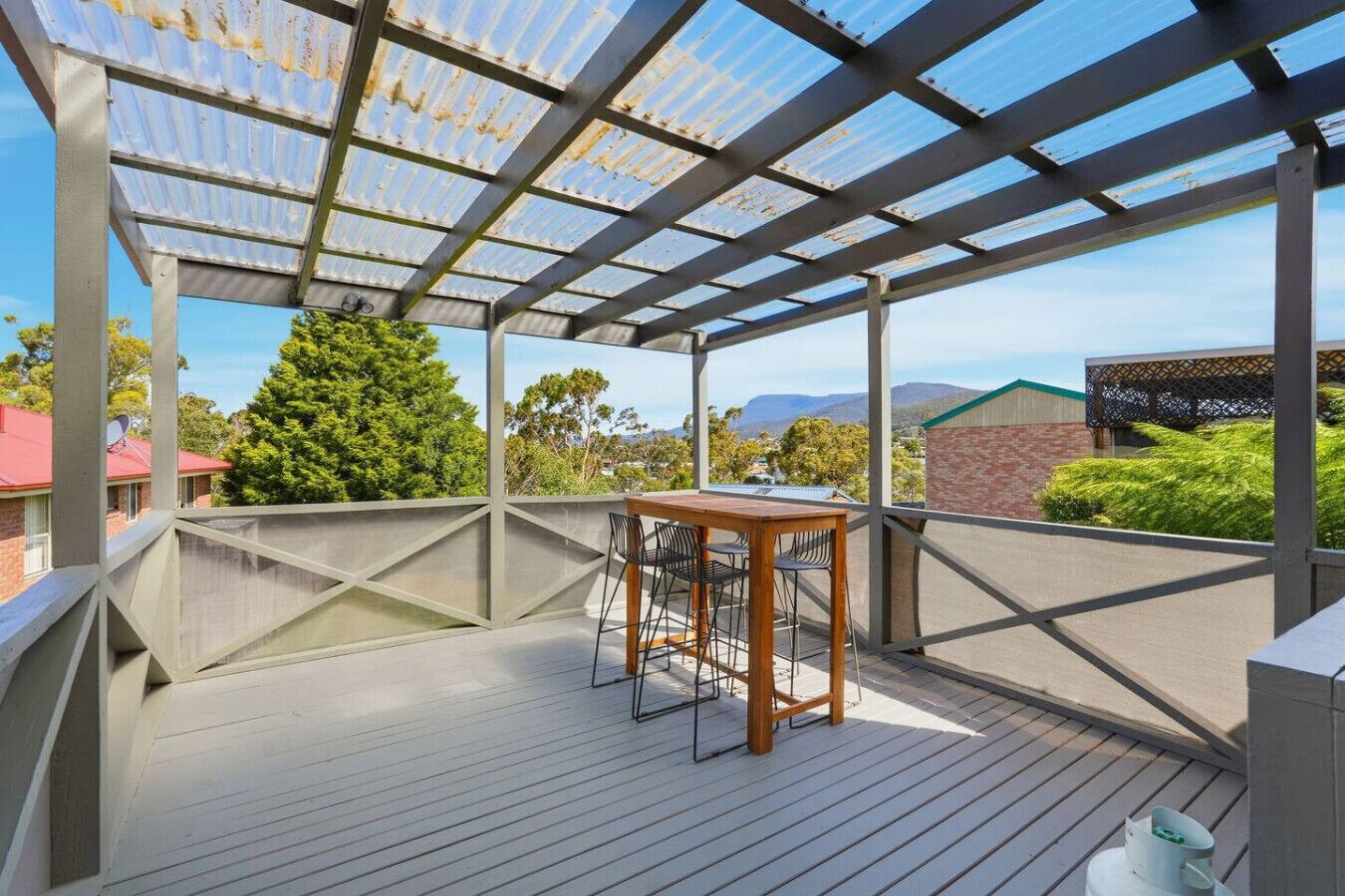 Ett takförsett utomhusområde med ett bord och stolar, utsikt över det omgivande landskapet och en pergola.