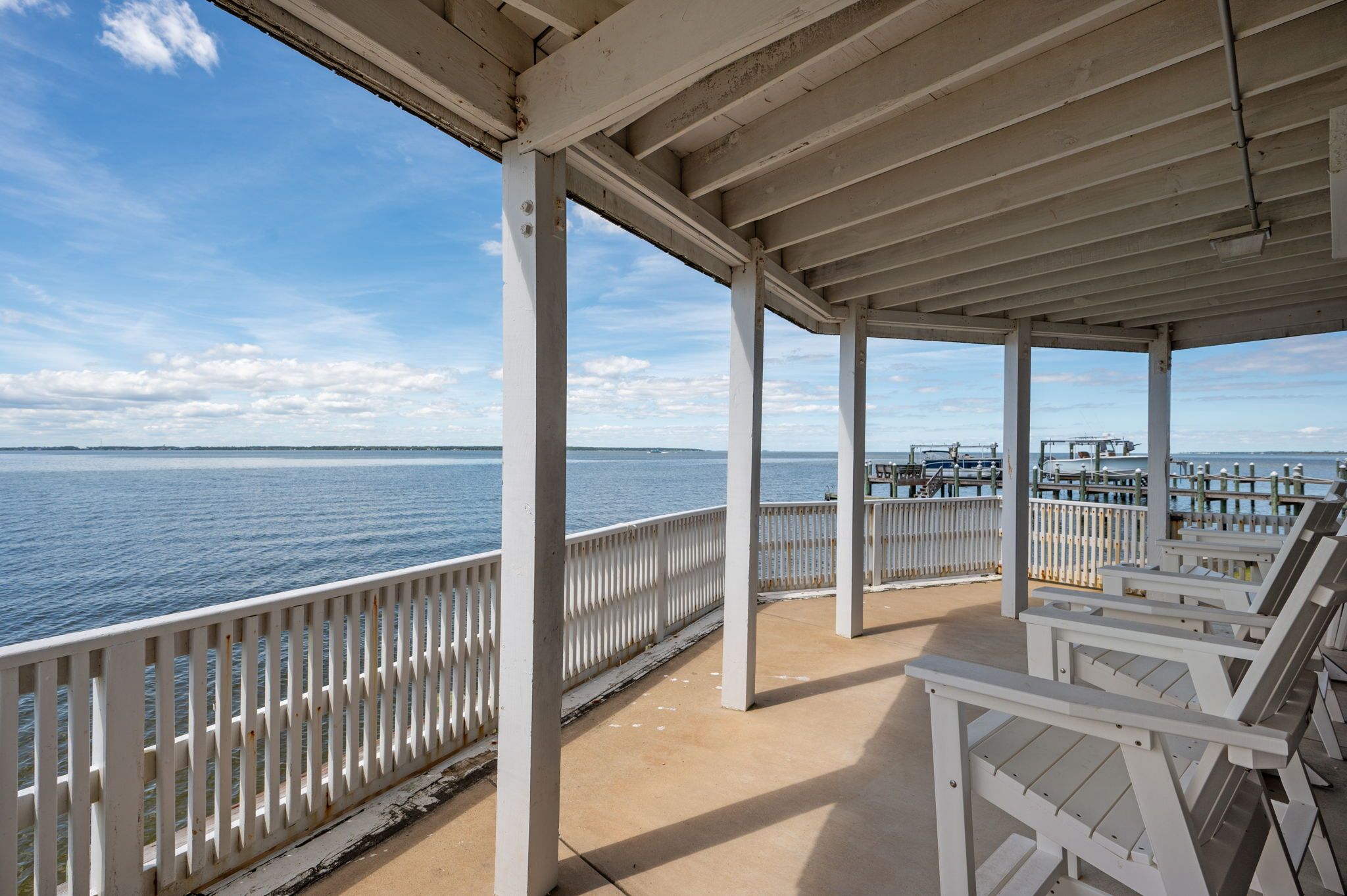 A covered outdoor area with a view of the water, featuring a white railing and benches.