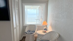 Una habitación con vistas al mar, sillas de mimbre, una lámpara y un televisor en la pared.