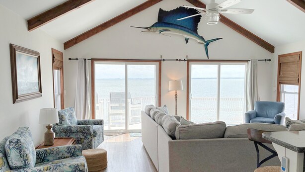 Un amplio salón con techo alto, ventilador de techo y un gran ventanal con vistas al mar.