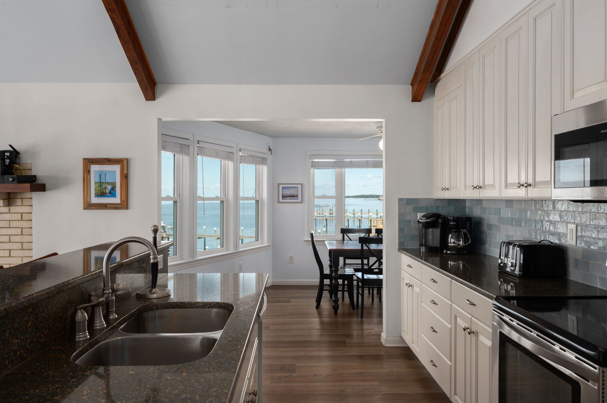 A modern kitchen with granite countertops, stainless steel appliances, and a view of the sea through large windows.