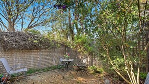 A backyard with a fenced area, a table with chairs, and a variety of plants and trees.