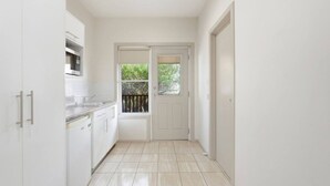 A narrow hallway with a kitchen area on the left, a double door at the end, and a view of greenery outside.