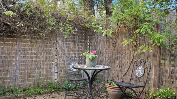 A round metal table with two chairs, surrounded by a bamboo fence and various plants.