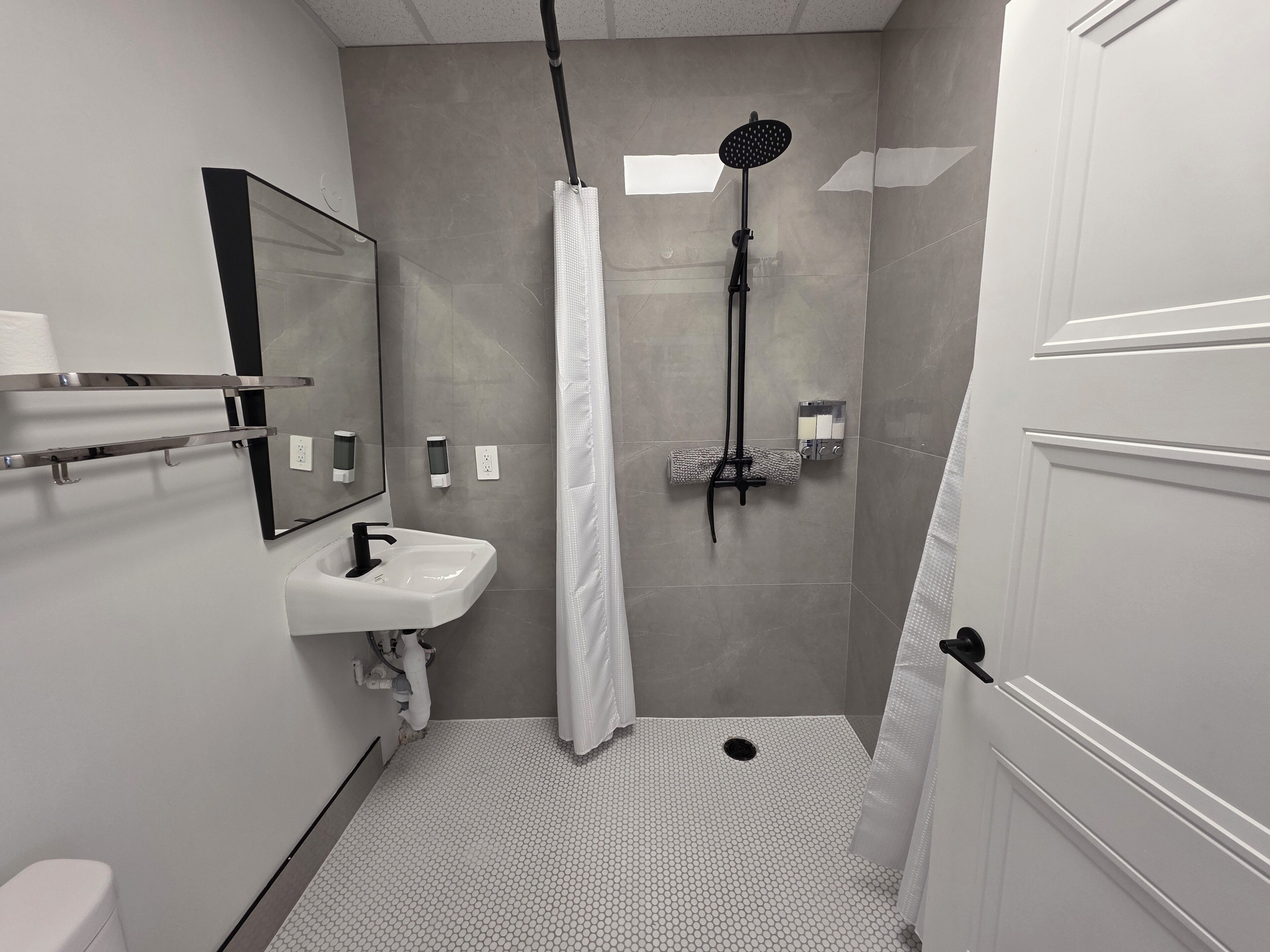 A bathroom with a shower, a sink, a toilet, and a mirror.