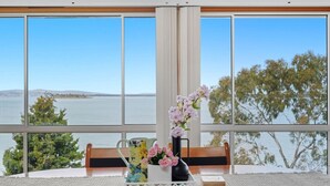 Una habitació amb grans finestres, una banca de fusta, una taula blanca i un ram de flors.
