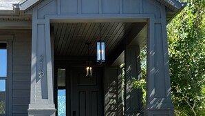 A residential house with a dark gray exterior, a front porch, and a visible door. - Bougie Basecamp: Heated Pool+Hot Tub+Sauna+Trails+Adventure Toy Rental Options (Lehi)