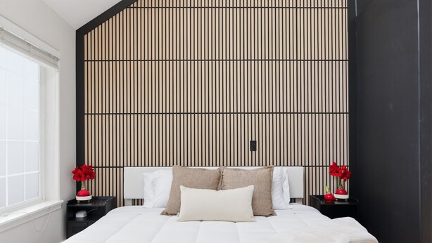Een moderne slaapkamer met een groot bed, een schuine plafond en een verticaal gestreept wand.