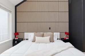 A modern bedroom with a large bed, a sloped ceiling, and a vertical striped wall. - Cozy King Bed, Private Bathroom and Entryway (Bend)