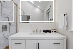 A modern bathroom with a white vanity, a large mirror, a shower, and a towel rack. - Cozy King Bed, Private Bathroom and Entryway (Bend)