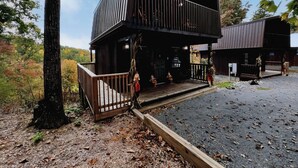 Una cabana rústica amb terrassa de fusta, un porxo cobert i vistes a la forest circumdant.
