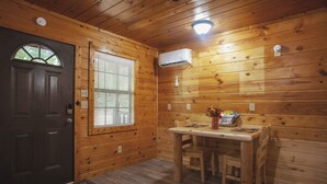 Interior d'una cabana de fusta amb una porta fosca, una finestra amb persianes, una taula amb caires i un aparell d'aire condicionat.