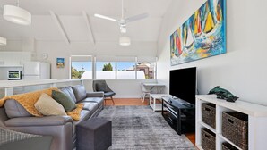 A modern living room with a sofa, a dining area, a TV, and a painting on the wall. - 2/16 Flinders Pde, Victor Harbor (Victor Harbor)