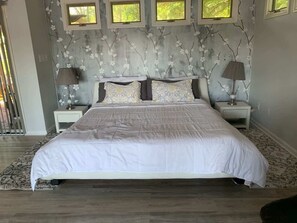 Une chambre avec un grand lit, deux tables de chevet avec des lampes, un mur décoré d’un motif et des fenêtres.
