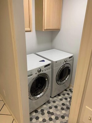 A laundry room with two front-loading washing machines and a dryer, wooden cabinets above, and a hexagonal patterned floor.