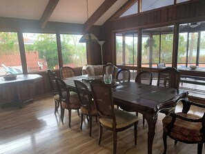Un espace repas comprenant une grande table en bois, six chaises et une vue sur l’extérieur grâce à de grandes fenêtres.