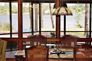 A dining area with a view of a lake, wooden furniture, and a hanging lamp.