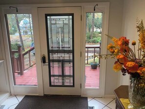 Une porte avec un panneau de verre, une terrasse rouge à l’extérieur et un vase rempli de fleurs sur la droite.