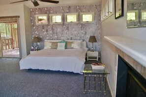 A bedroom with a bed, bedside tables, a fireplace, and a window with blinds.
