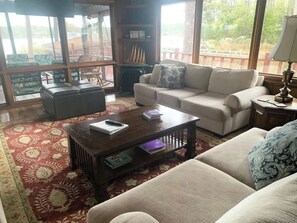 Un salon comprenant un canapé, une table basse et un tapis. Une fenêtre offre une vue sur la verdure à l’extérieur.
