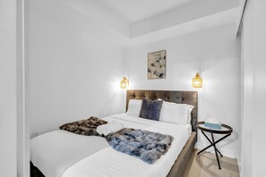 A modern hotel room with a large bed, two bedside tables, and a wall-mounted light fixture. - Downtown Toronto CN Tower Condo (Toronto)