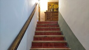 Una escalera con peldaños rojos, barandal de madera y un armario de madera con un jarrón de flores.