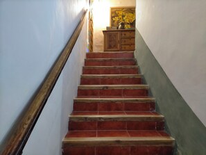 Una escalera con peldaños rojos, barandal de madera y un armario de madera con un jarrón de flores.