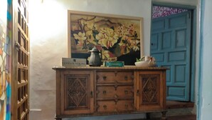 Un mueble de madera con cajones, un cuadro de flores y una puerta azul al fondo.