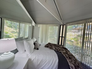 A hotel room with a bed, a lamp, a view through the window, and a door. - Canopy Seven: Tree Top - Pools - Pickleball - near Golf (Lake Ozark)