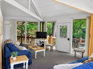 A furnished living room with a television, a sofa, a coffee table, and a view of a deck and greenery. - Canopy Seven: Tree Top - Pools - Pickleball - near Golf (Lake Ozark)