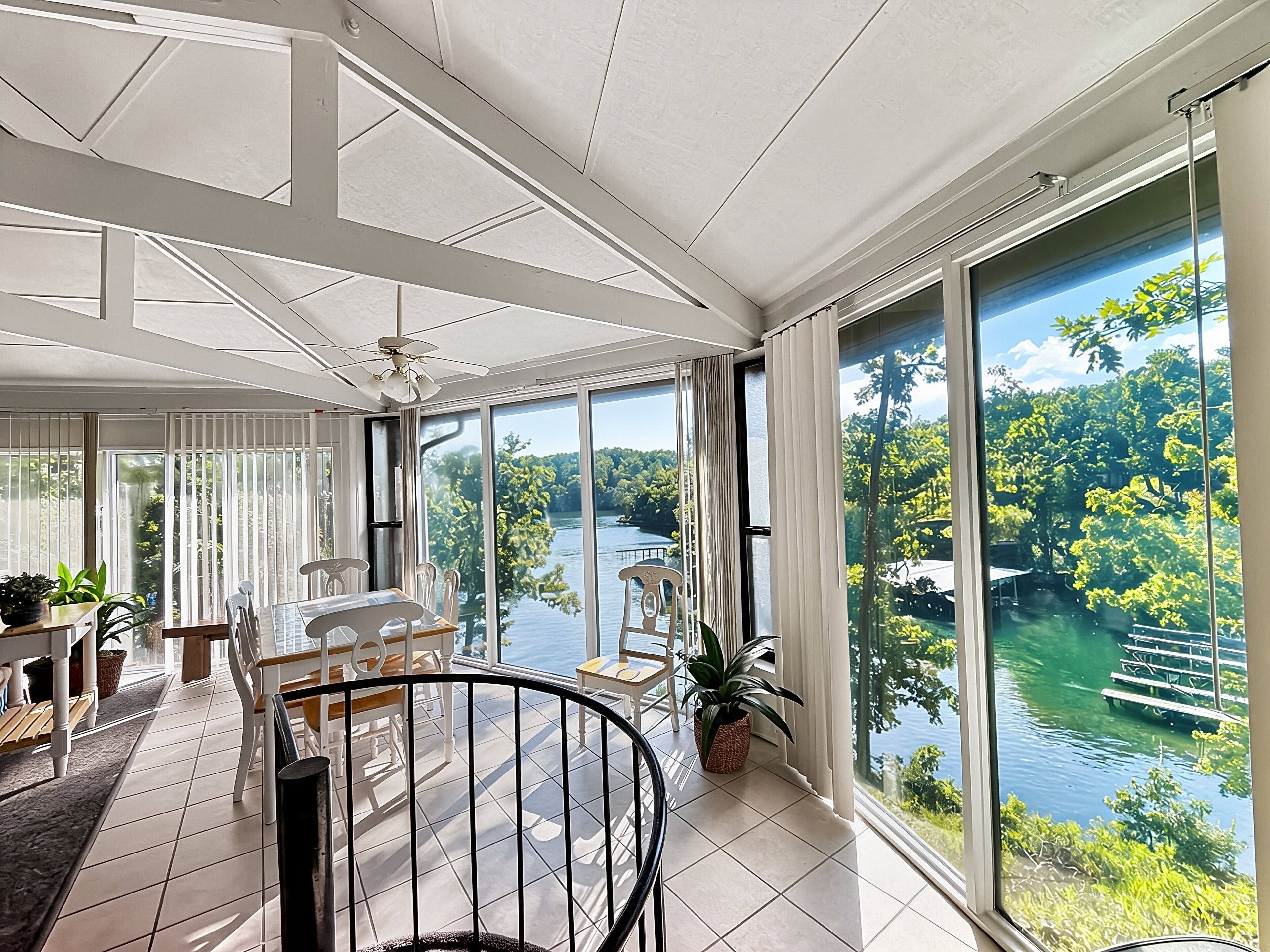 Un'ampia stanza con una grande finestra vista lago, un'area pranzo con sedie e tavolo, e una ventola a soffitto.