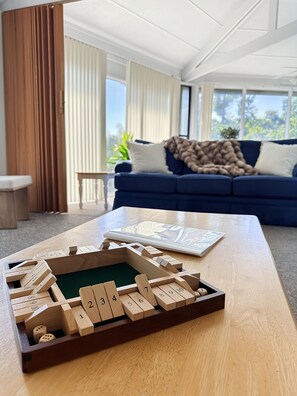 A wooden board game on a table in a room with a blue sofa, a window with curtains, and a plant. - Canopy Seven: Tree Top - Pools - Pickleball - near Golf (Lake Ozark)