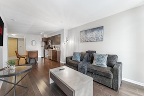 A modern living room with a sofa, coffee table, and a dining area with a glass table. - The Vine & View Suite (Toronto)