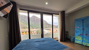 A room with a bed, a window with a view of mountains, and a blue curtain. - DIEGUITO'S HOUSE IN THE SACRED VALLEY (Cusco)