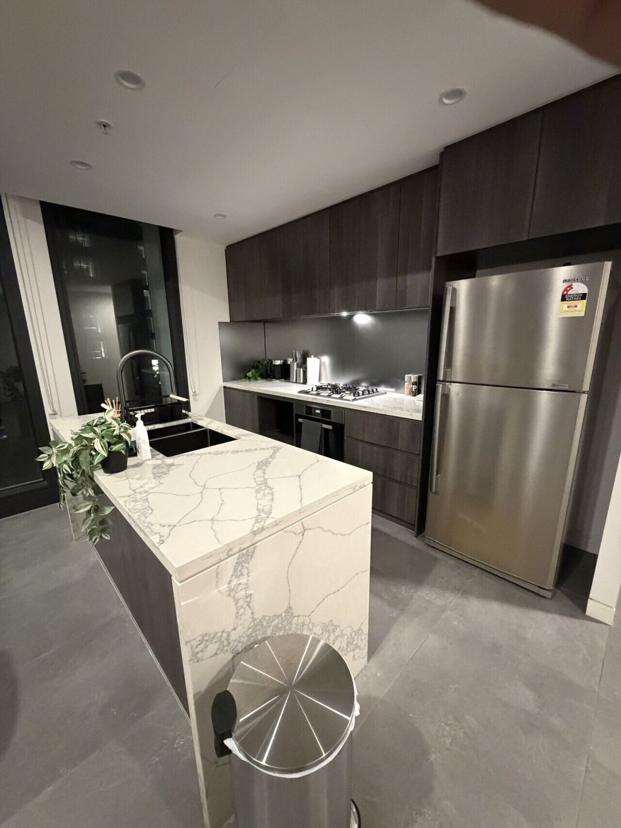 A modern kitchen with a central island, stainless steel appliances, and dark cabinetry.