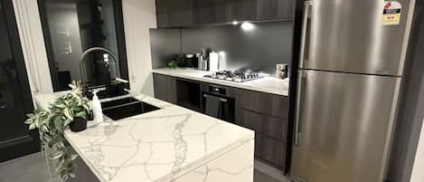 Cocina moderna con una isla central, electrodomésticos de acero inoxidable y armarios oscuros.