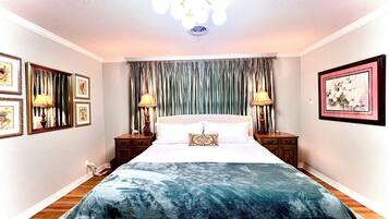 A bedroom with a large bed, two bedside tables with lamps, a chandelier, and framed artwork on the walls.