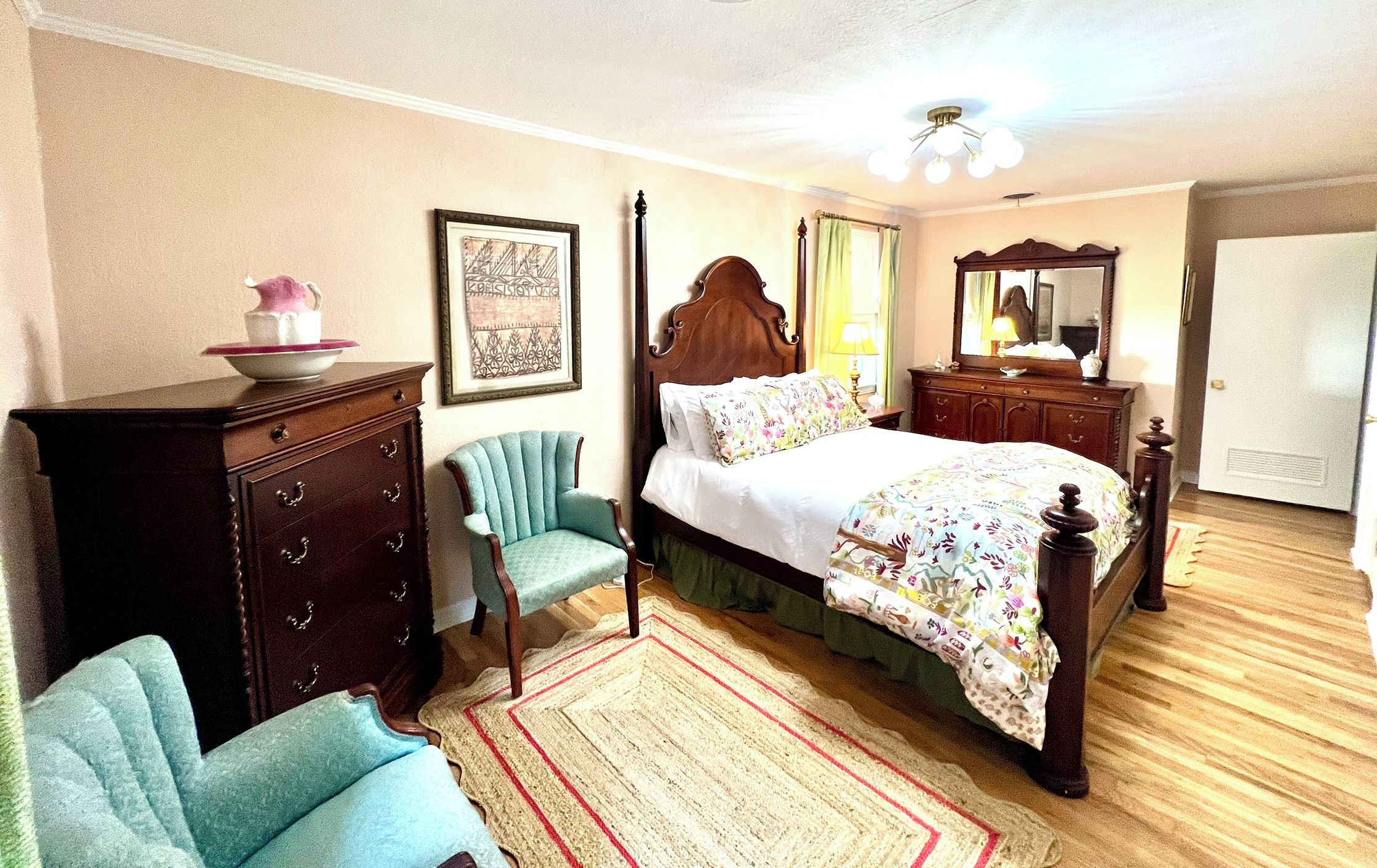 Un dormitorio con cama con dosel, cómoda, silla, alfombra y espejo.