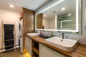 Een moderne badkamer met een houten wastafel, twee wasbakken, een grote spiegel en een wasmachine.
