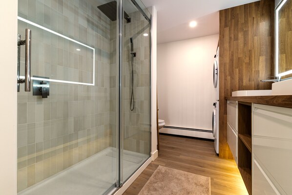 Een moderne badkamer met een douchecabine van glas, een houten wastafelmeubel en een wit toilet.