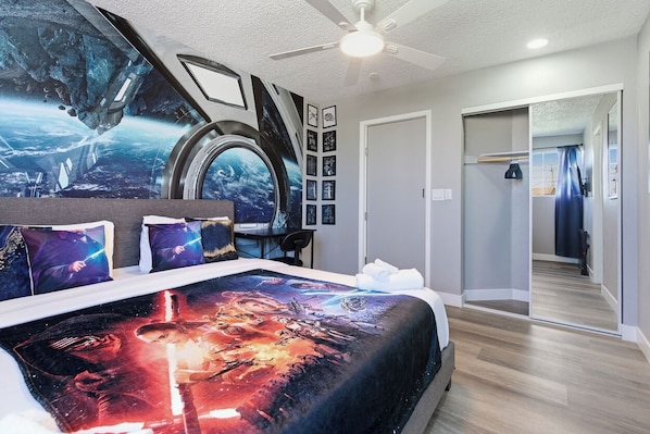 Ein Schlafzimmer mit einem großen Bett, das mit einer himmelshartigen Bettdecke ausgestattet ist, einem Deckenventilator und Blick auf einen Flur mit Spiegel und Tür.