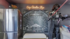 Une chambre sur le thème de Star Wars, avec une statue de Dark Vador, un panneau lumineux au néon, une grande fresque murale de Star Wars, un réfrigérateur moderne en acier inoxydable et un banc.