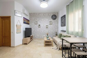 Ein Wohnzimmer mit Fernseher, Sofa, Couchtisch aus Holz und einem Esstisch mit Bänken.