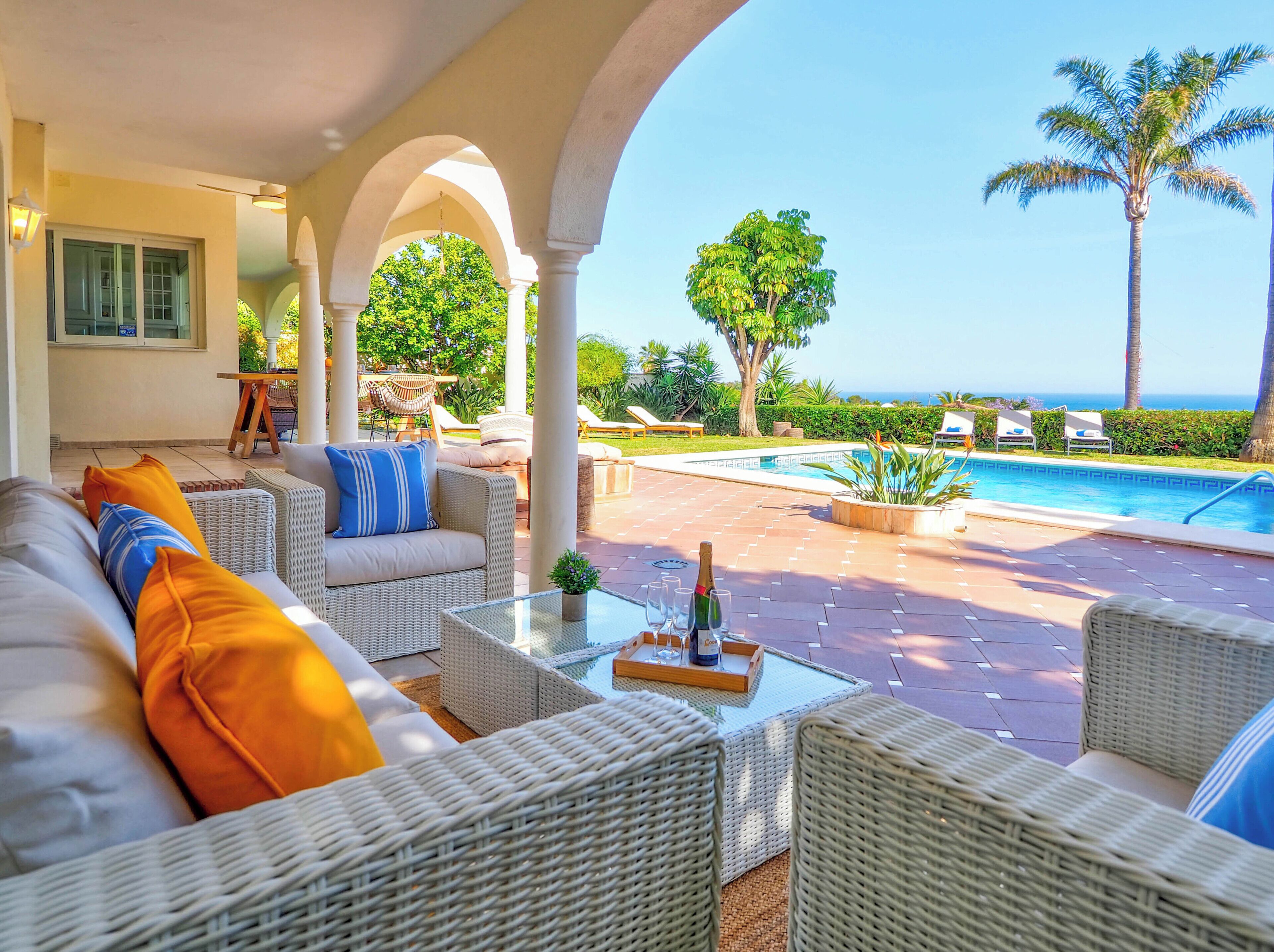 A covered outdoor seating area with wicker furniture, a pool, and a view of the ocean.